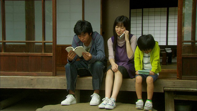 日本东京，女孩在打电话，男孩在看书，男孩在玩电子游戏，坐在家门口视频素材