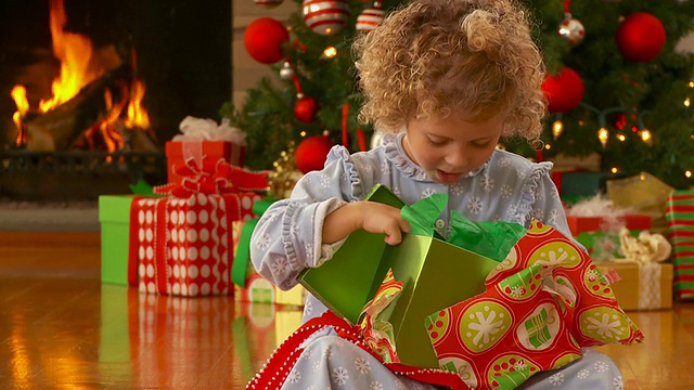 女孩(4-5岁)穿着睡衣坐在地板上，打开圣诞礼物，壁炉和圣诞树的背景，弗吉尼亚州里士满视频素材