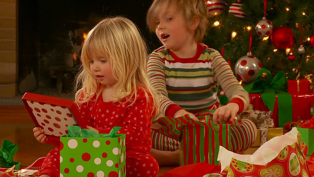 男孩(6-7)和女孩(2-3)穿着睡衣坐在地板上，打开圣诞礼物，里士满，弗吉尼亚州，美国视频素材