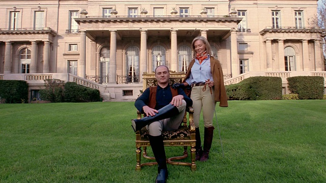 大宅前身穿骑马服的富豪夫妇(男子坐在椅子上)的广角照片视频素材