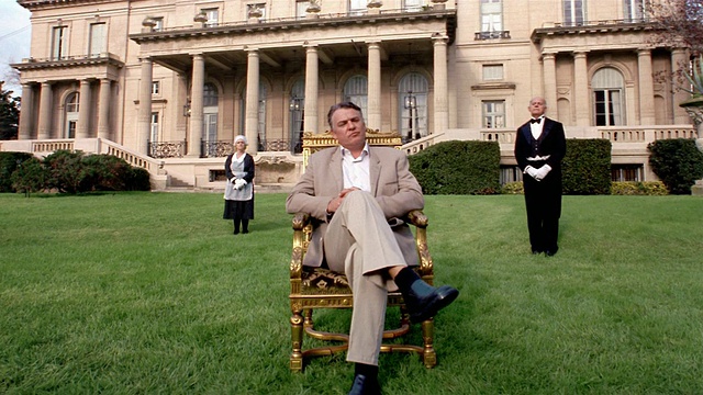 一个男人坐在镀金的椅子上，仆人们在大厦前立正视频素材