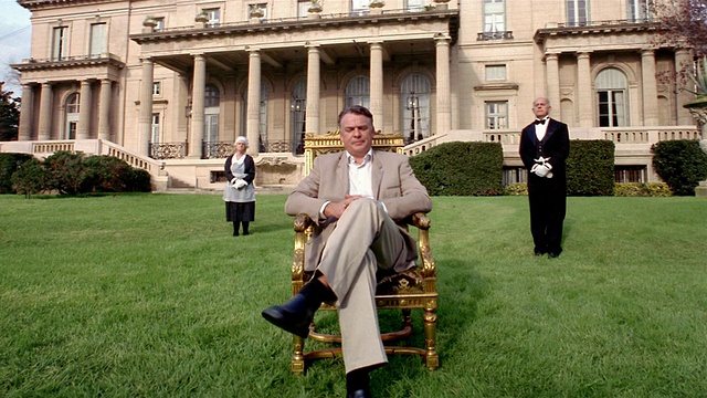 一个男人坐在镀金的椅子上，仆人们在大厦前立正视频下载