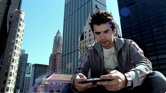 在一个阳光明媚的日子里，在曼哈顿金融区/纽约市玩手持视频游戏的年轻人视频素材