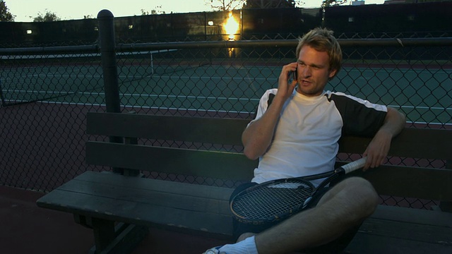 美国加州圣巴巴拉，一名年轻人坐在网球场的长椅上，正在打手机视频素材