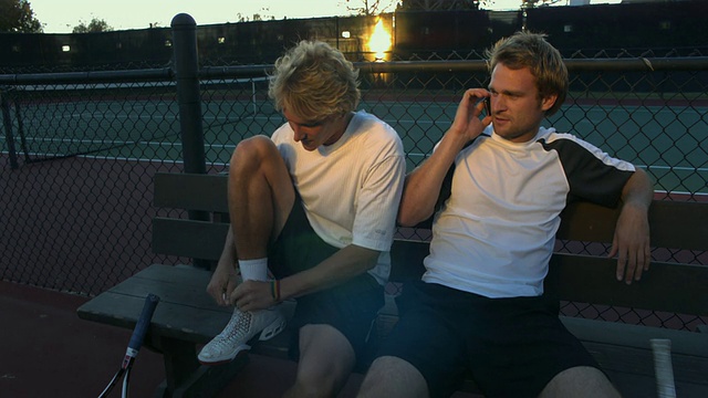两位年轻男子坐在网球场的长椅上，其中一人正在打手机，美国加州圣巴巴拉视频素材