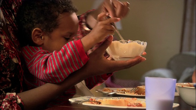 在餐桌上坐在妈妈膝盖上吃东西的小孩/在食物上放帕尔马干酪视频下载