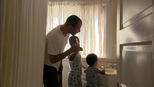 透过浴室门口的中景，父亲和两个年幼的儿子在早上刷牙视频素材