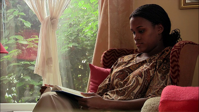 中镜头倾斜的女人坐在窗户旁边的椅子上看书视频素材