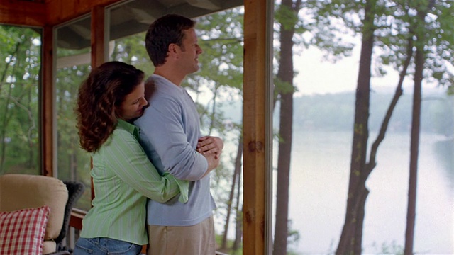 中拍摄的夫妇拥抱和看湖从门廊的湖屋视频下载