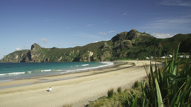 海浪拍打海岸时，坐在海滩上的人/新西兰北部视频下载
