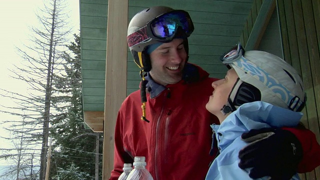 在美国蒙大拿州白鱼山小屋前，一对穿着滑雪装备的情侣喝着瓶子里的水，亲吻着视频素材
