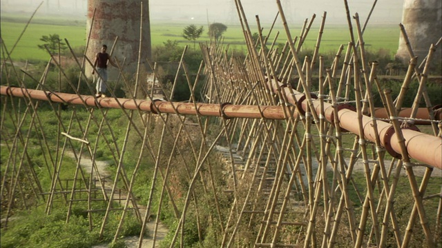 孟加拉国，男子站在地上用竹竿支撑的管子上视频下载