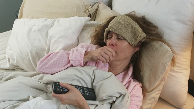 美国亚利桑那州菲尼克斯市，一名女子在床上咳嗽，额头上抱着垃圾塔，用电视遥控器视频下载