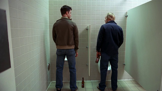 宽镜头两个男人拿着啤酒瓶在用小便池/男人盯着另一个男人视频下载