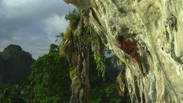 男子赤足攀爬岩壁，将绳子扣进钩环，手浸在白垩袋里。泰国甲米视频素材