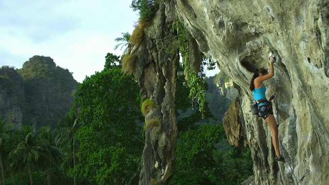 泰国甲米，女攀岩者伸手将绳索插入岩壁上的钩环，正在攀爬视频素材