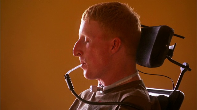 一名四肢瘫痪的年轻男子坐在特殊轮椅上，对着镜头微笑，并用话筒移动轮椅/新斯科舍省哈利法克斯视频下载