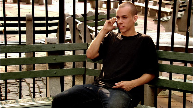 纽约马丁·f·特纳赫游乐场，一个中等身材的年轻人坐在长椅上打电话视频素材