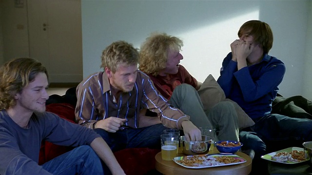 中镜头拍摄了四个年轻人坐在沙发上看电视/跳起来欢呼/倒在沙发上视频素材