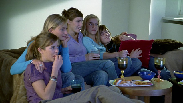 中镜头摄影车拍摄了五个坐在沙发上看电视/吃喝的女人视频下载