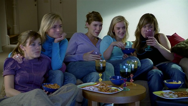 中拍摄影车拍摄了五个坐在沙发上看电视/吃喝/聊天+大笑的女人视频素材