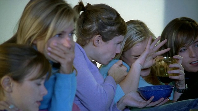 5个女人坐在沙发上看恐怖电影，畏畏缩缩地跳着，捂着眼睛视频素材