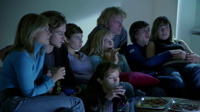 中景摄影拍摄了一群坐在沙发上看电视或吃零食的男女视频素材