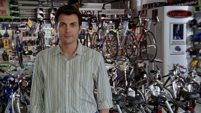 中景缩小人像男子站在自行车店的自行车架前/放大在CAM微笑的男子视频素材