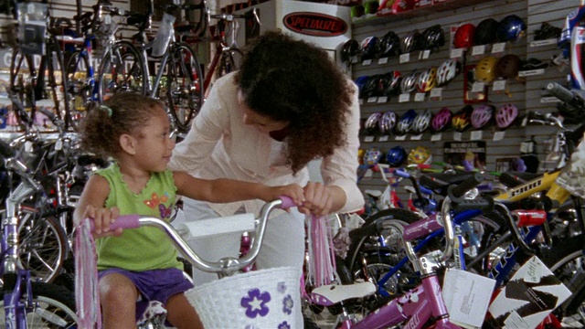 中等镜头的女人和骑着自行车的小女孩说话/售货员过来提供帮助视频素材
