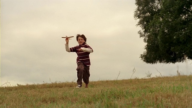 中等射击的男孩跑过一个田野，带着玩具飞机/投掷飞机，看着它飞视频素材