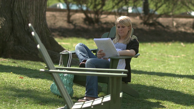 在美国宾夕法尼亚州伯利恒的校园草坪上，一名年轻男子坐在女学生旁边的躺椅上使用手机视频下载
