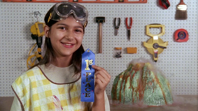 中镜头女孩摆着蓝色的丝带，旁边是火山喷发的模型视频下载