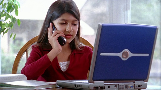中镜头放大缩小女孩一边用手机聊天一边用笔记本电脑做作业视频素材