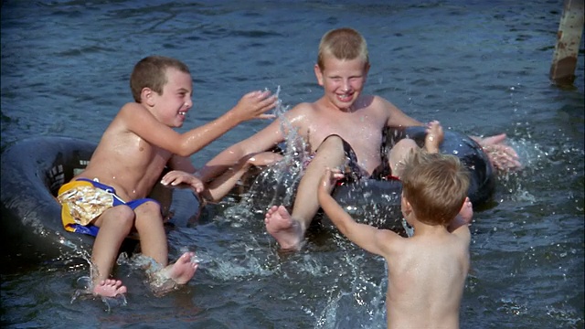 慢镜头:三个男孩在内胎里漂浮，互相溅起水花/纽约银湖视频素材