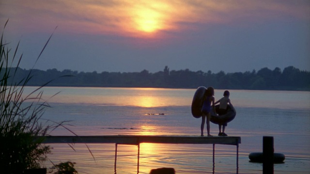 慢镜头，三个孩子带着内胎奔跑，在日落时分从码头上跳入湖中视频下载