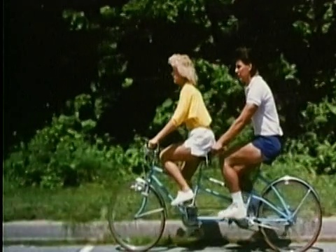 1987年，宽镜头跟踪拍摄了在青翠背景下骑双人自行车的男女视频下载