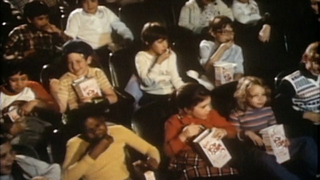1985年高角度中拍摄的青少年在电影院看电影/拿着爆米花盒视频下载