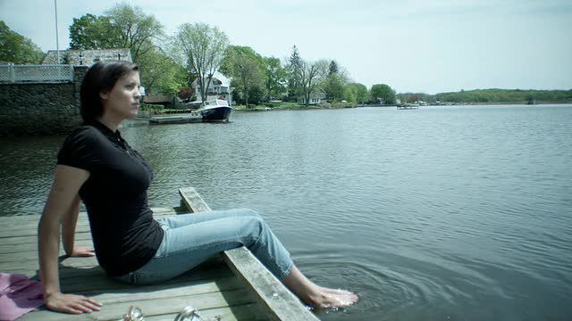 美国康涅狄格州埃塞克斯，一名年轻女子坐在码头上，脚浸在水里视频素材
