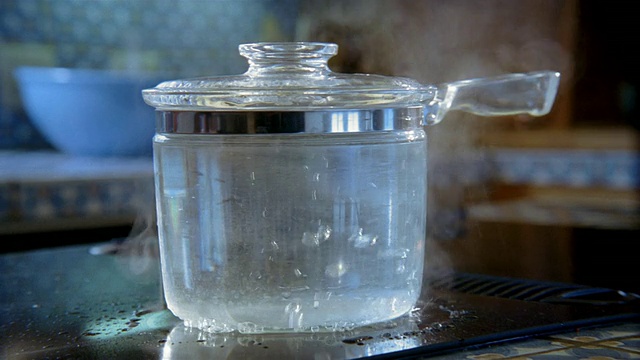 靠近在电炉上有盖的玻璃锅里沸腾的水/手移开盖子视频素材