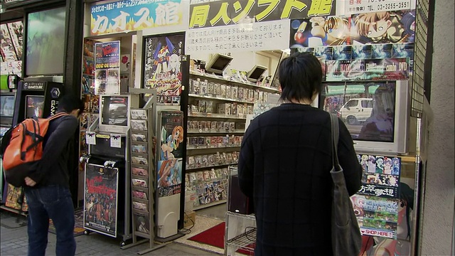 在秋叶原区/东京游戏店前玩电子游戏的年轻男子的广角后视图视频下载