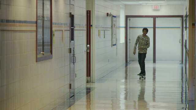 WS男孩(12-13)沿着学校走廊玩滑板，老师从其他方向来，美国纽约卡泽诺维亚视频素材