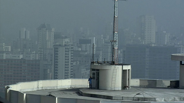 一名男子在建筑物屋顶上行走，背景是天际线/巴西圣保罗视频下载