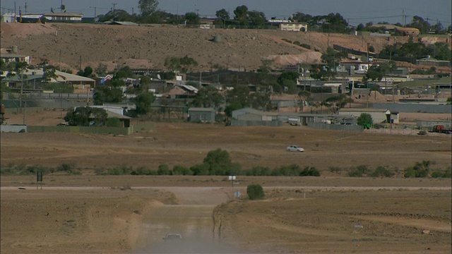 WS TU后视图白色越野车行驶在尘土飞扬的道路上，城镇和树的背景，库伯佩迪，南澳大利亚，澳大利亚。视频素材