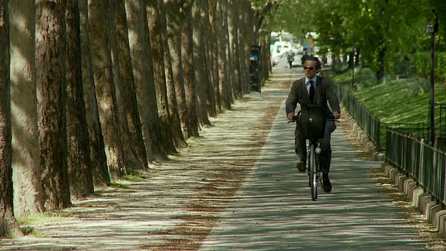 法国巴黎，商人骑着自行车沿着绿树成荫的小路走向摄影机视频素材