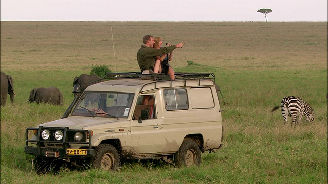 宽镜头夫妇在狩猎通过双筒望远镜从天窗看动物4x4 /马赛马拉，肯尼亚视频素材