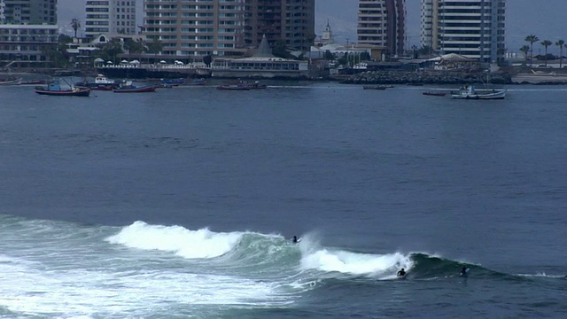 在智利伊基克，在海浪上冲浪的男子，背景中的建筑视频下载