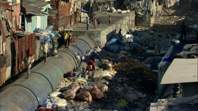 印度马哈拉施特拉邦孟买，贫民窟里的大水管和成堆的垃圾，背景是现代建筑视频下载