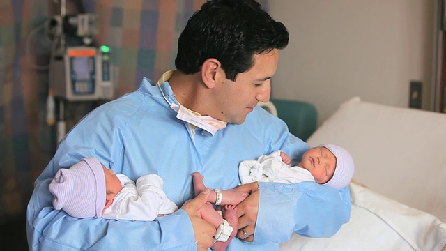 图为一位父亲抱着刚出生的双胞胎微笑着抬头看/美国弗吉尼亚州里士满视频素材