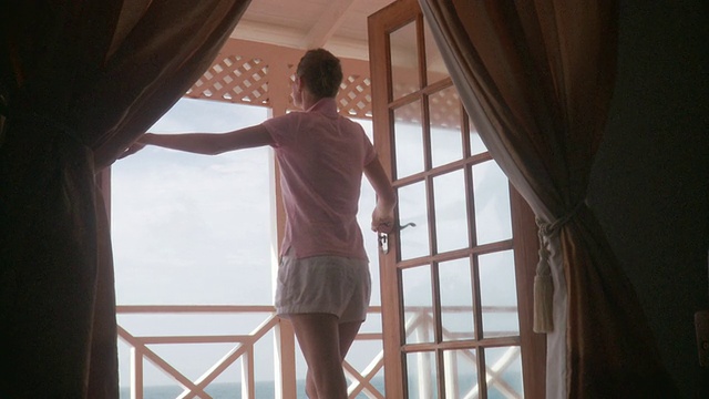 一名年轻女子打开双扇门，站在阳台上眺望大海/斯卡伯勒，特立尼达和多巴哥视频下载