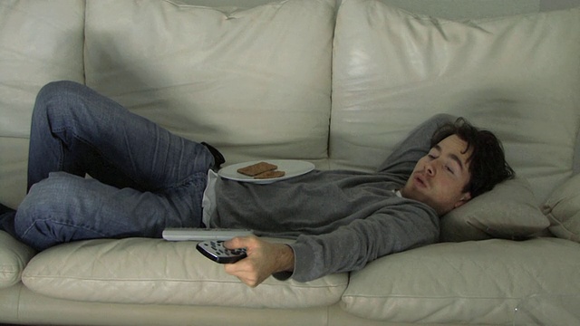 年轻人躺在沙发上，看电视/哈克尼，英国视频素材